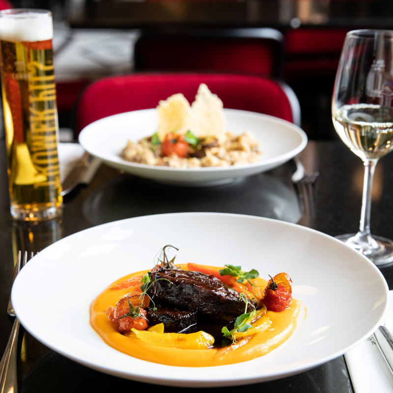 Hauptspeisen auf dem Tisch, geschmortes Kalbs-Schulterscherzel mit Süßkartoffel-Püree, Risotto im Hintergrund, ein Glas Bier und ein Glas Weißwein